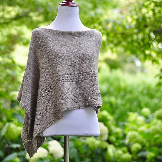 Knitted poncho on a mannequin against a green outdoor background